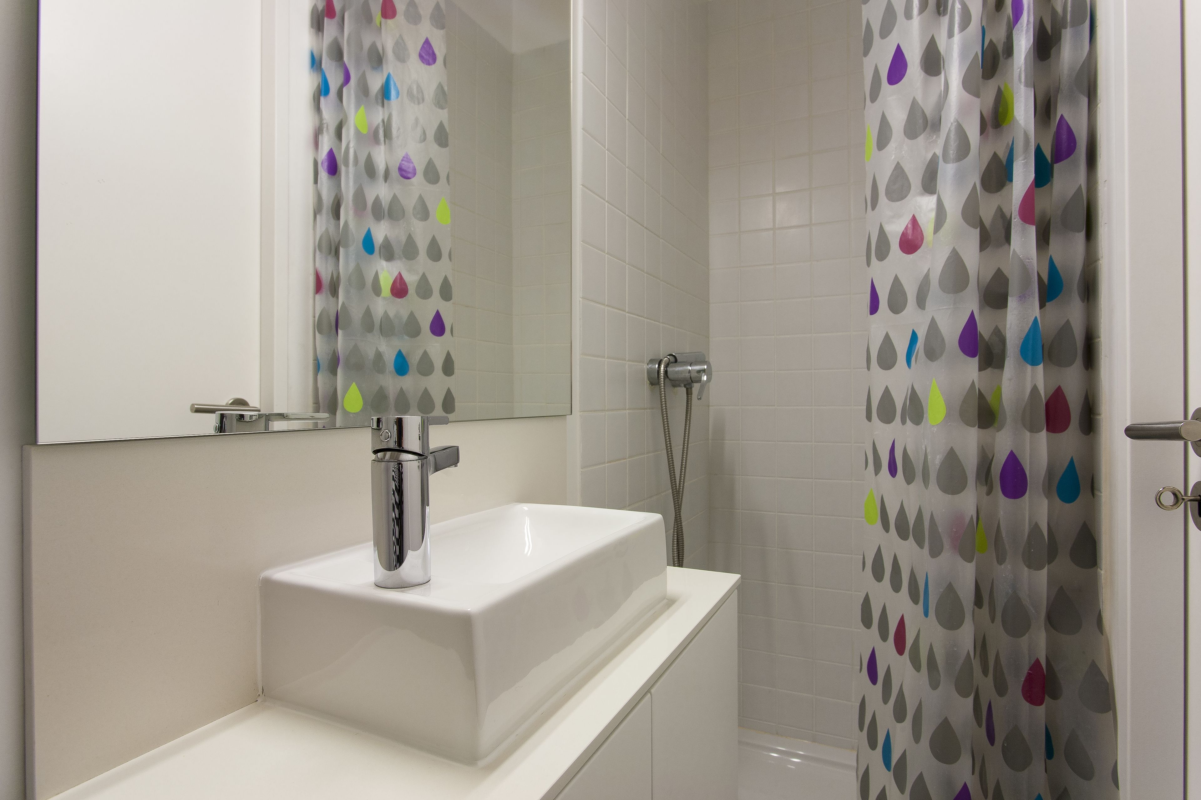A bathroom with a white sink, a mirror, and a shower with a colorful shower curtain.