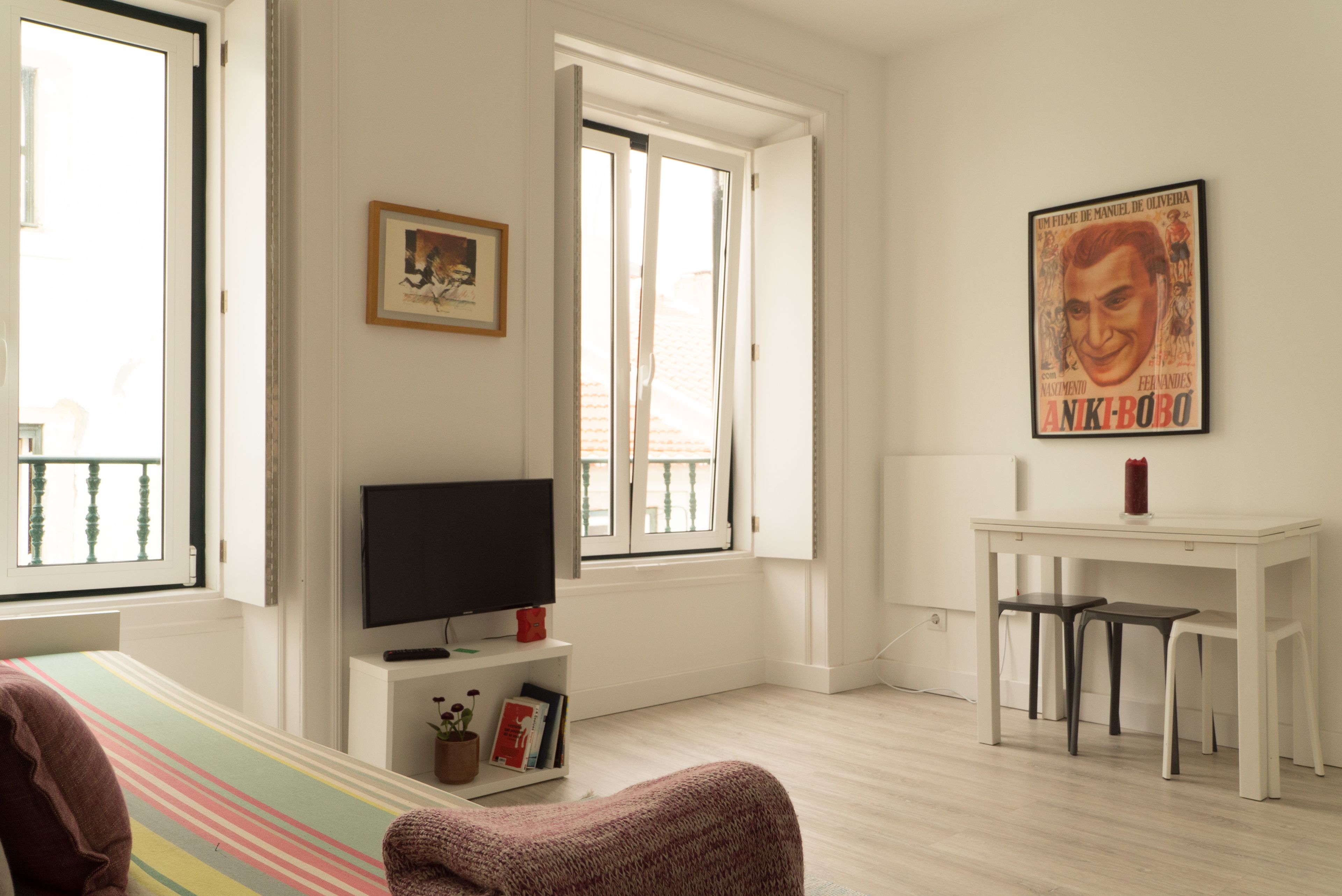 A bright living room with a TV, a framed picture, and a poster on the wall.