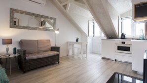 A modern kitchen with white cabinetry, a dining area with a wicker sofa, and a large mirror on the wall. - Severa Apartments (Lisbon)
