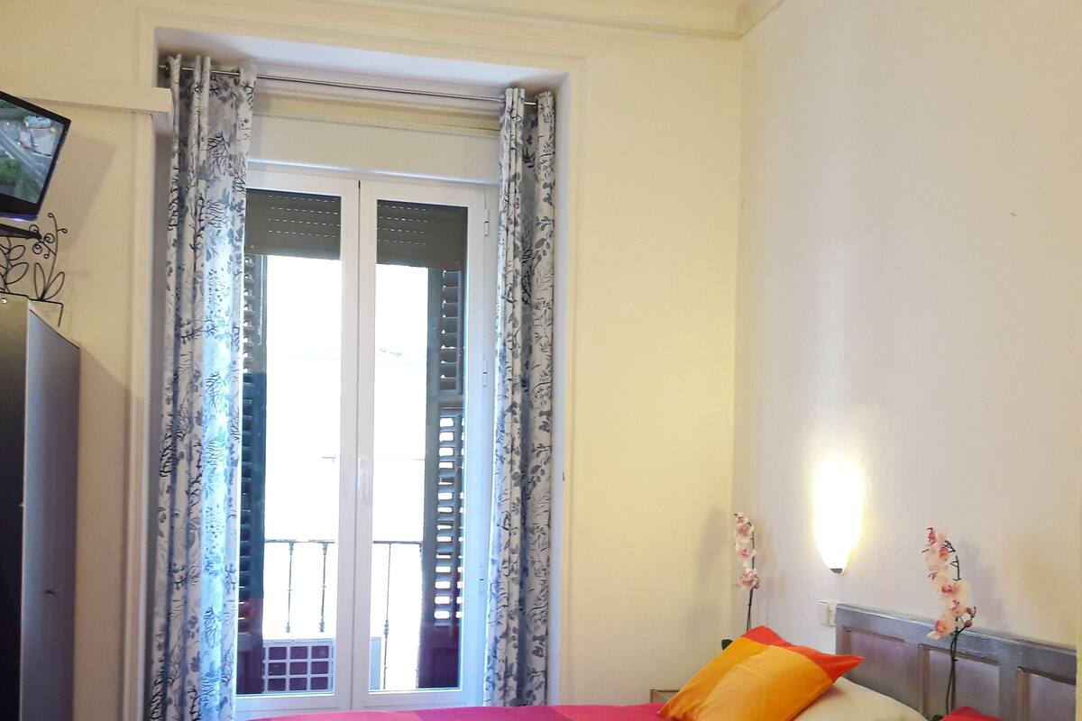 A hotel room with a bed, a TV, and a window with curtains.