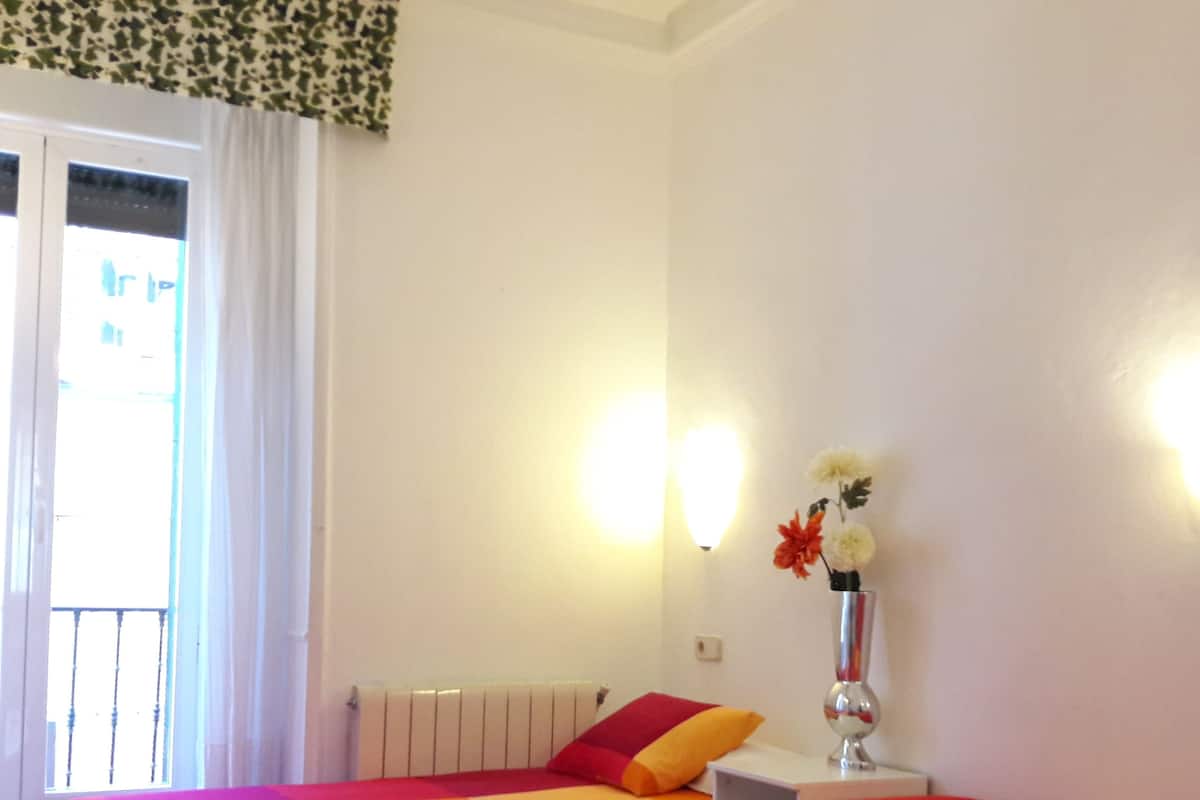 A hotel room with two beds, a nightstand, a vase with flowers, and a window with curtains.