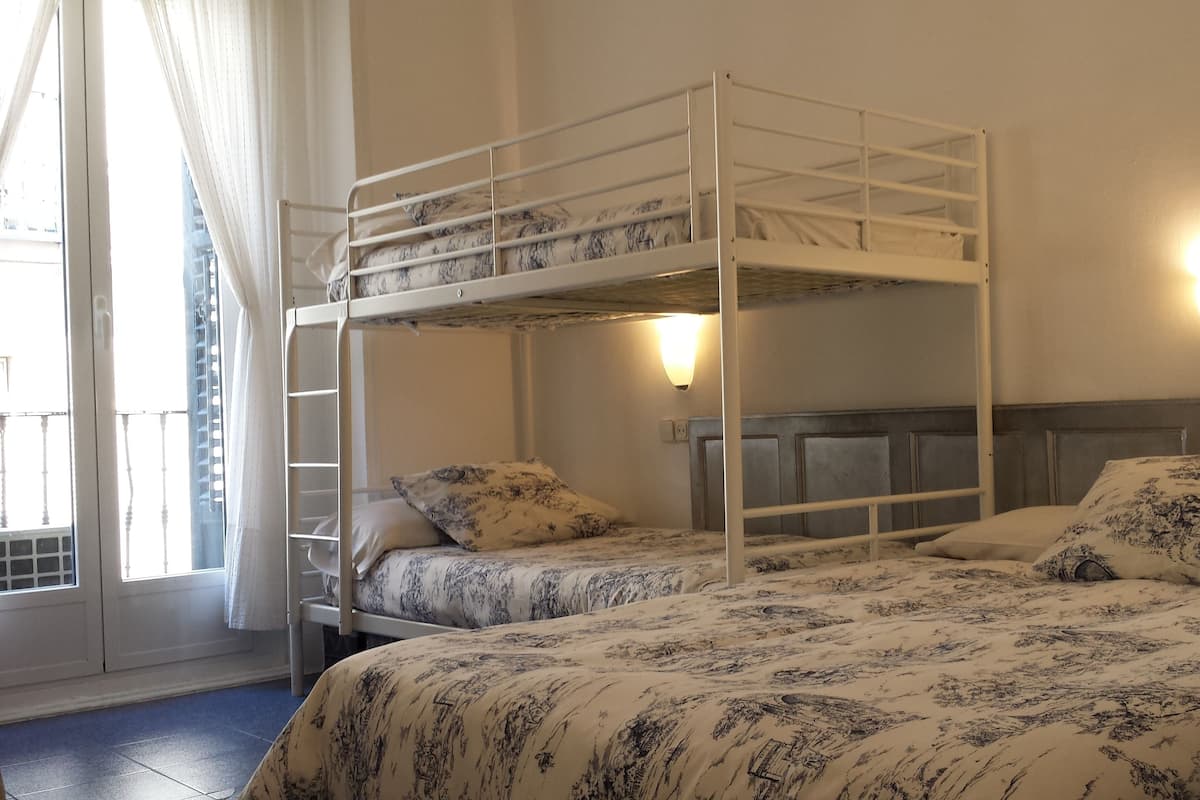 A bunk bed room with two beds, each with floral-patterned bedding. There are two wall-mounted lights and a window with curtains.