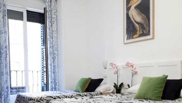 A bedroom with a bed, a window with curtains, a painting, and a potted orchid. - Hostal Casa Chueca (Madrid)