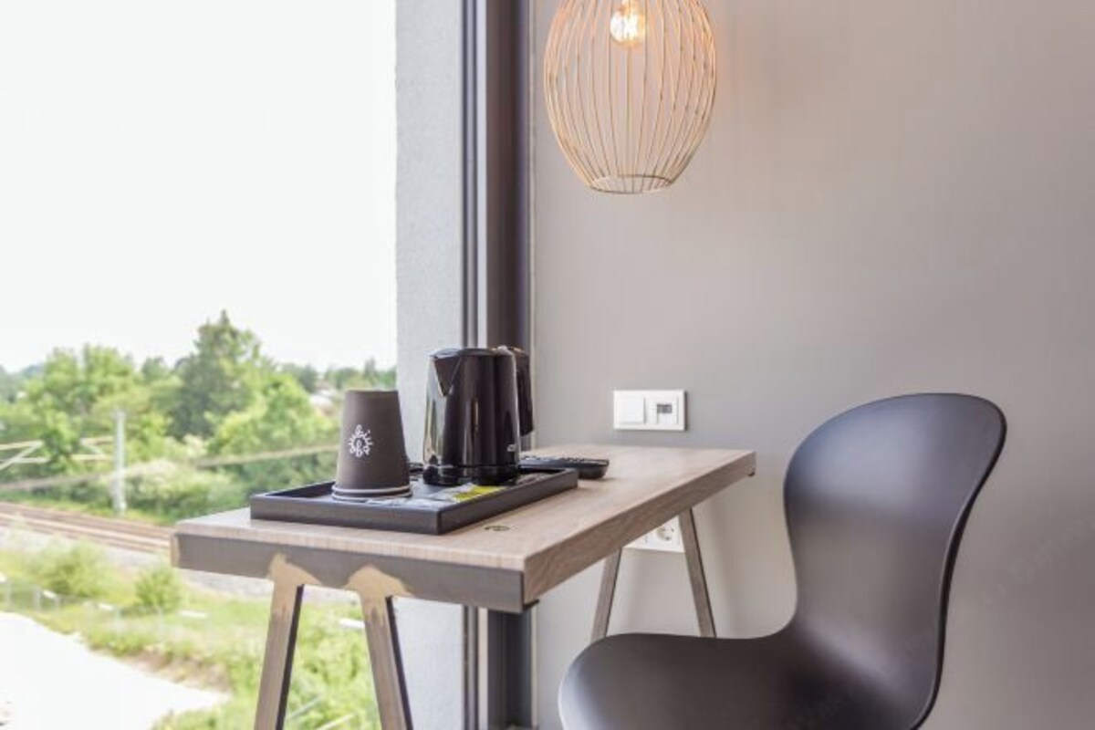 Una habitación moderna con un escritorio de madera, una silla negra, una cafetera y una lámpara colgante.