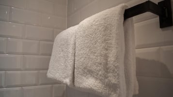 A white towel hanging on a black towel rack in a bathroom with white tiled walls.