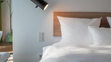 Una cama bien hecha con ropa blanca, cabecera de madera y lámpara fijada a la pared.