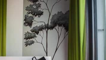 A room with a bed, a black mug on the headboard, a book on a side table, and green curtains.