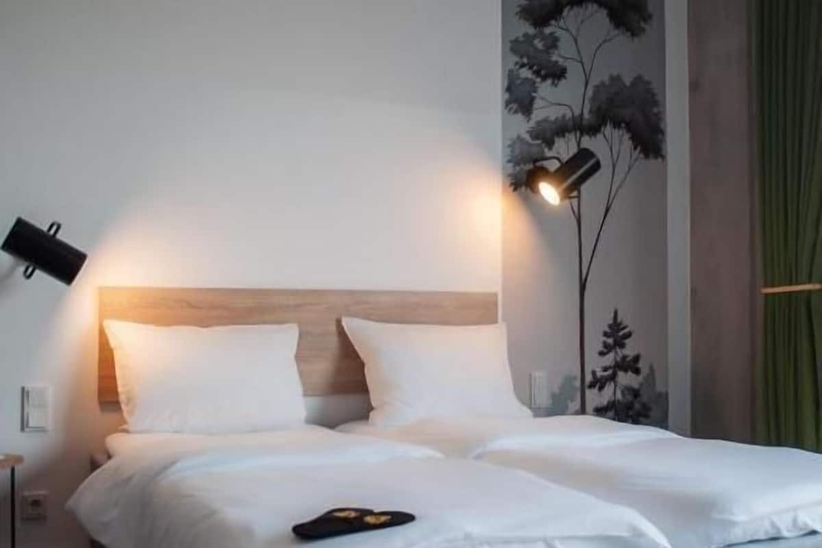 Een tweepersoonsbed met een grijs hoofdeinde, twee bedlampen en een aan de muur bevestigde televisie.