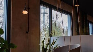 Una sala de estar moderna con un sofá, dos otomanos amarillos, una lámpara colgante y un ventanal con vistas.