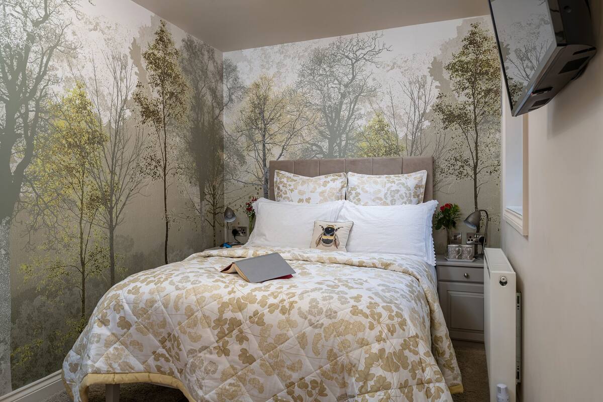 A bedroom with a bed, a nightstand, a lamp, and a wall-mounted air conditioner.