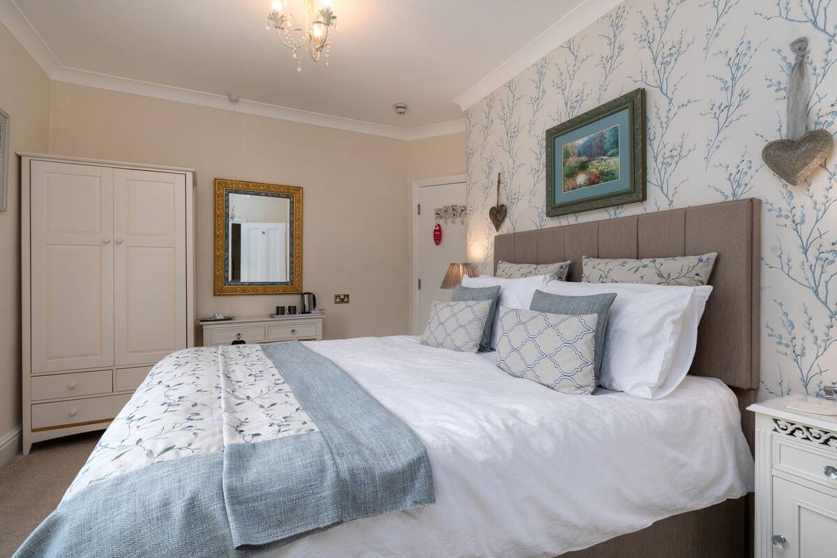 A bedroom with a large bed, a dresser, a wardrobe, and a mirror.