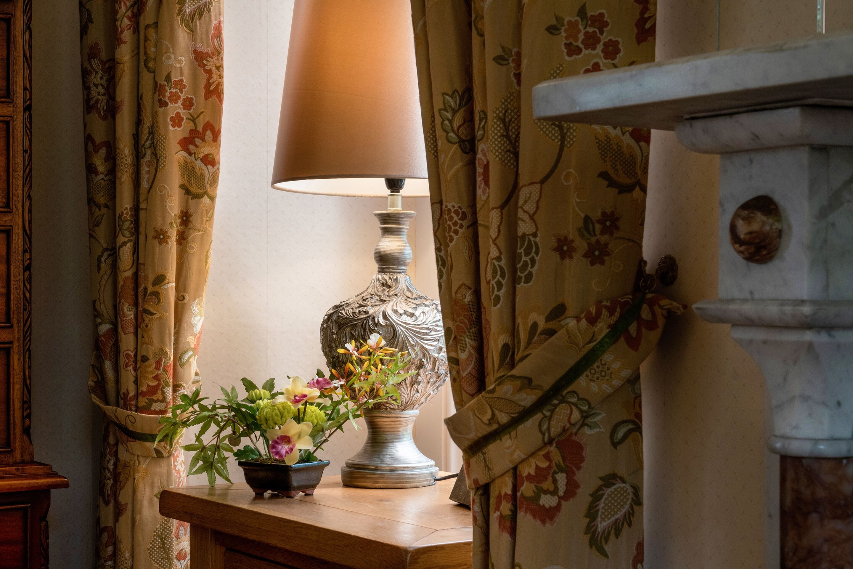 A table with a lamp and a floral arrangement.