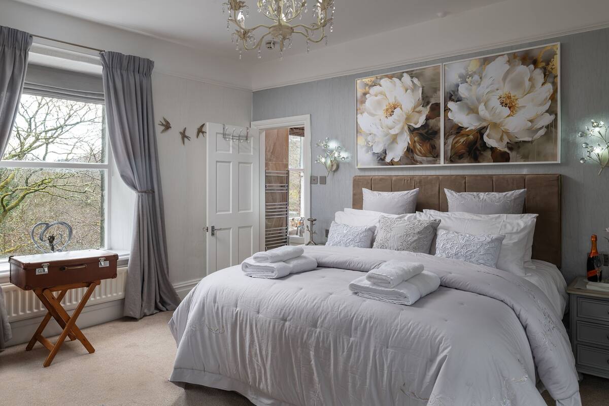 A bedroom with a large bed, a dresser, a window with curtains, and a painting on the wall.