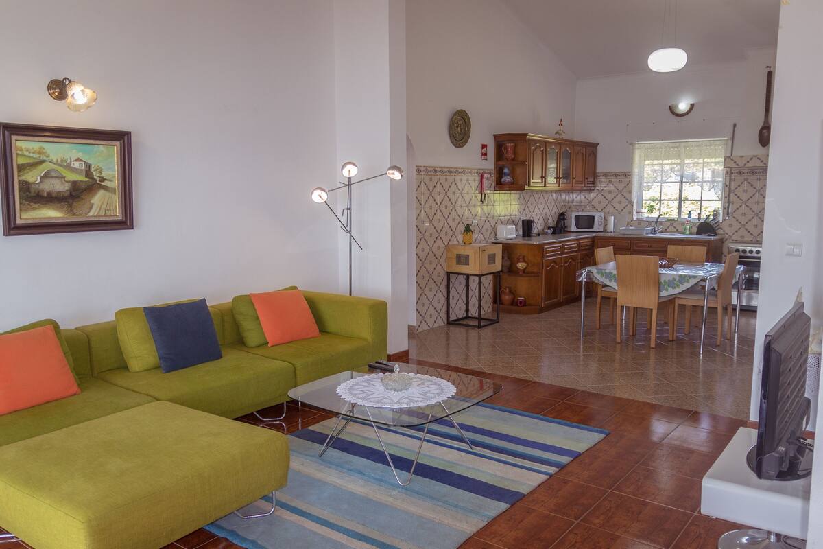A living room with a green sofa, a coffee table, and a kitchen area in the background.