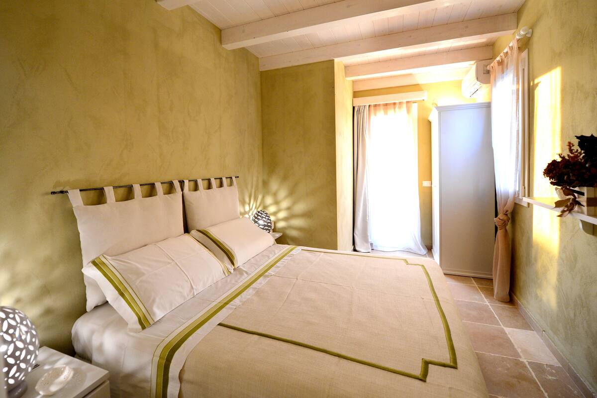 Un dormitorio con cama, mesita de noche y ventana con cortinas.