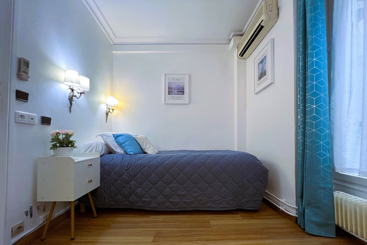 Un dormitorio pequeño y ordenado con cama, mesita de noche, lámpara y un cuadro en la pared.