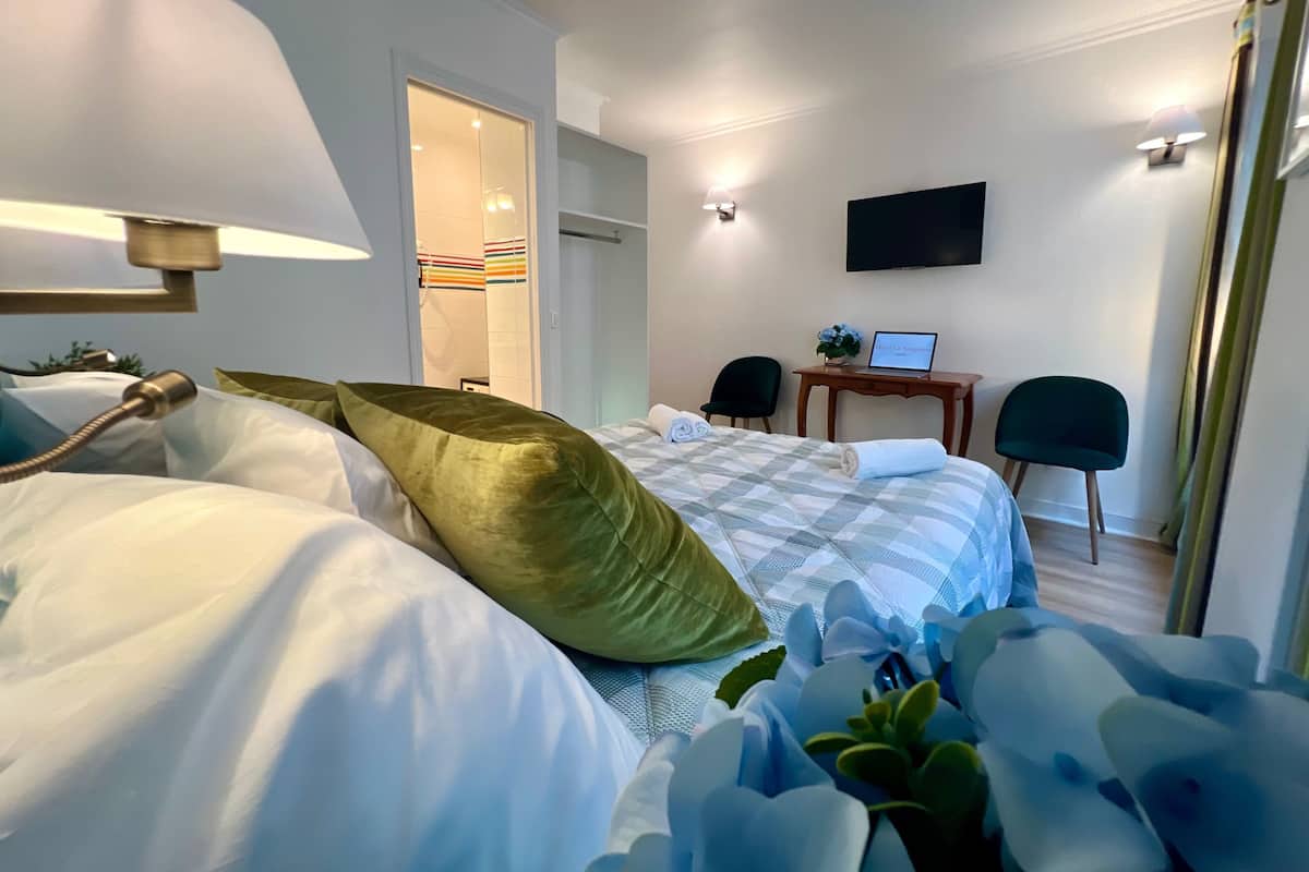 Una habitación de hotel con cama, escritorio, computadora portátil, silla y televisor en la pared.