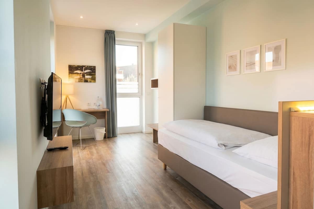 A modern hotel room with a bed, desk, chair, and a television.