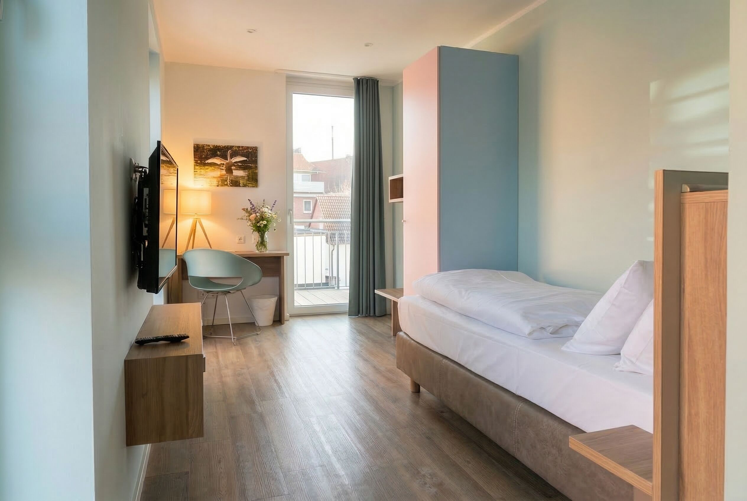 A hotel room with a bed, a desk, a chair, a TV, and a balcony with a view.
