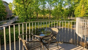 A balcony with a glass table and wicker chairs, surrounded by greenery and a metal railing. - Steverbett Hotel (Luedinghausen)