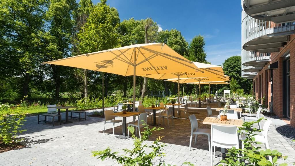 Un patio al aire libre con mesas y sillas, rodeado de follaje y árboles.