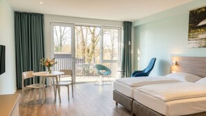 A hotel room with a bed, a desk, a chair, a table, and a balcony with a view of trees. - Steverbett Hotel (Luedinghausen)