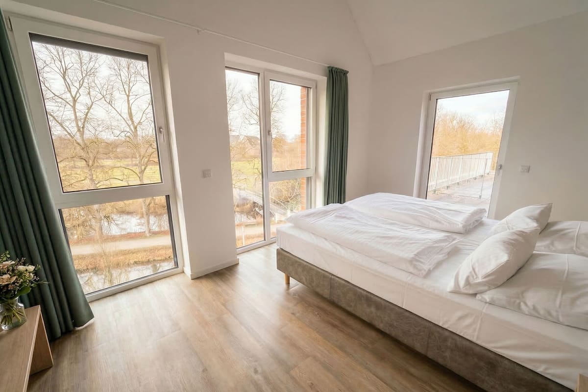 A bedroom with a large bed, two windows, and a view of the outdoors.