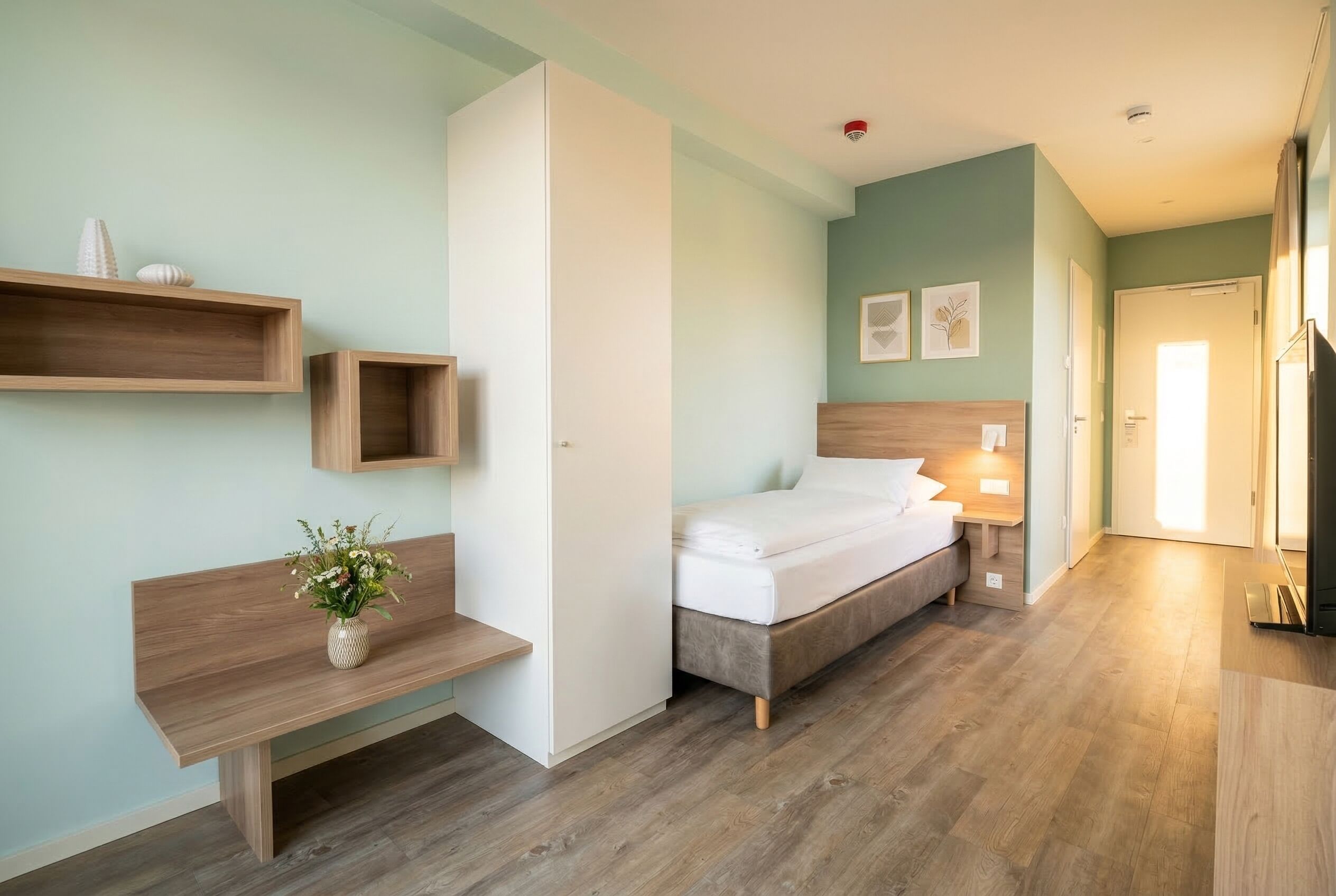 Un dormitorio con cama, mesita de noche, estantes en la pared y una lámpara de noche.