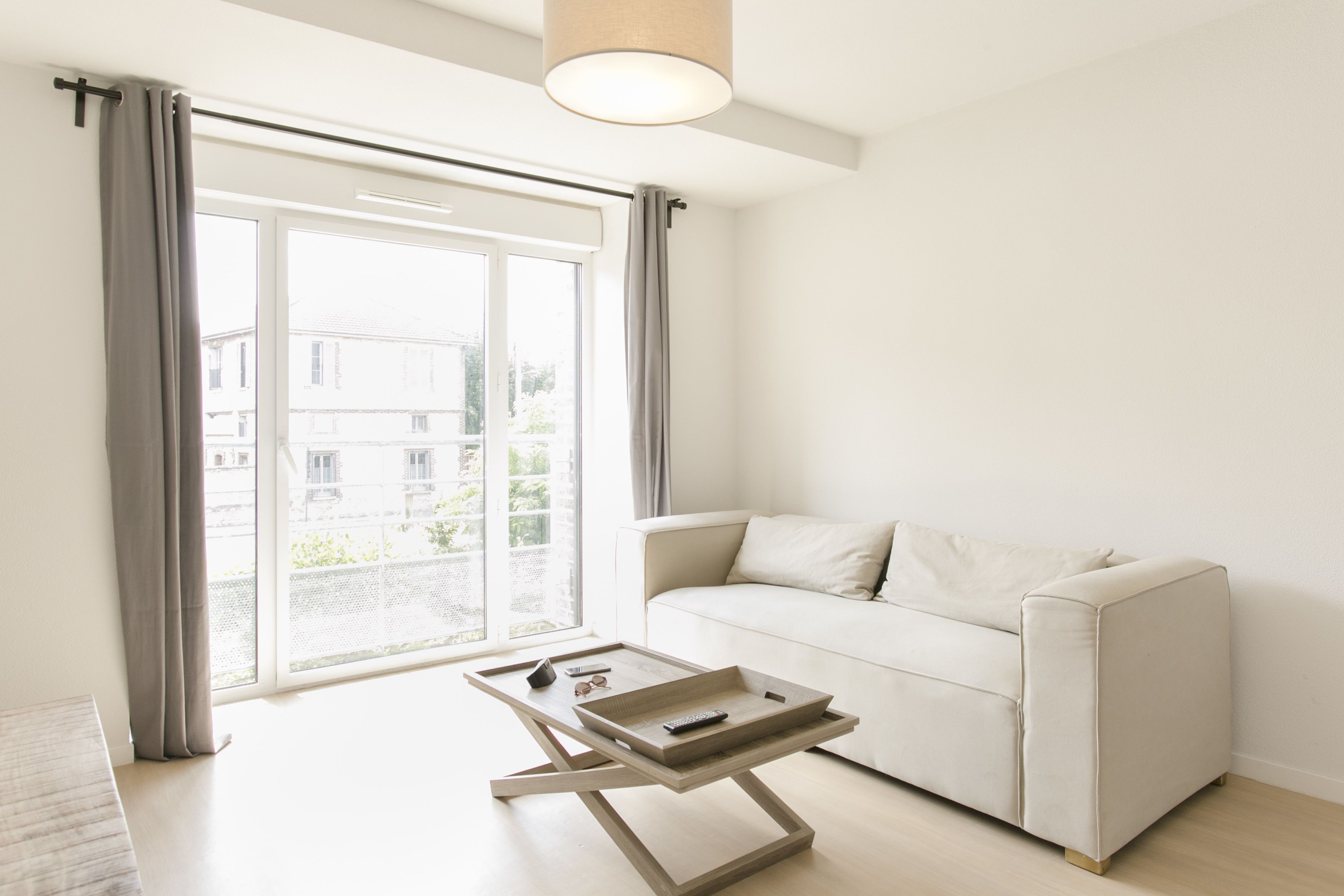 Un salon moderne avec un canapé blanc, une table basse en bois et une grande porte-fenêtre coulissante donnant sur un espace extérieur.