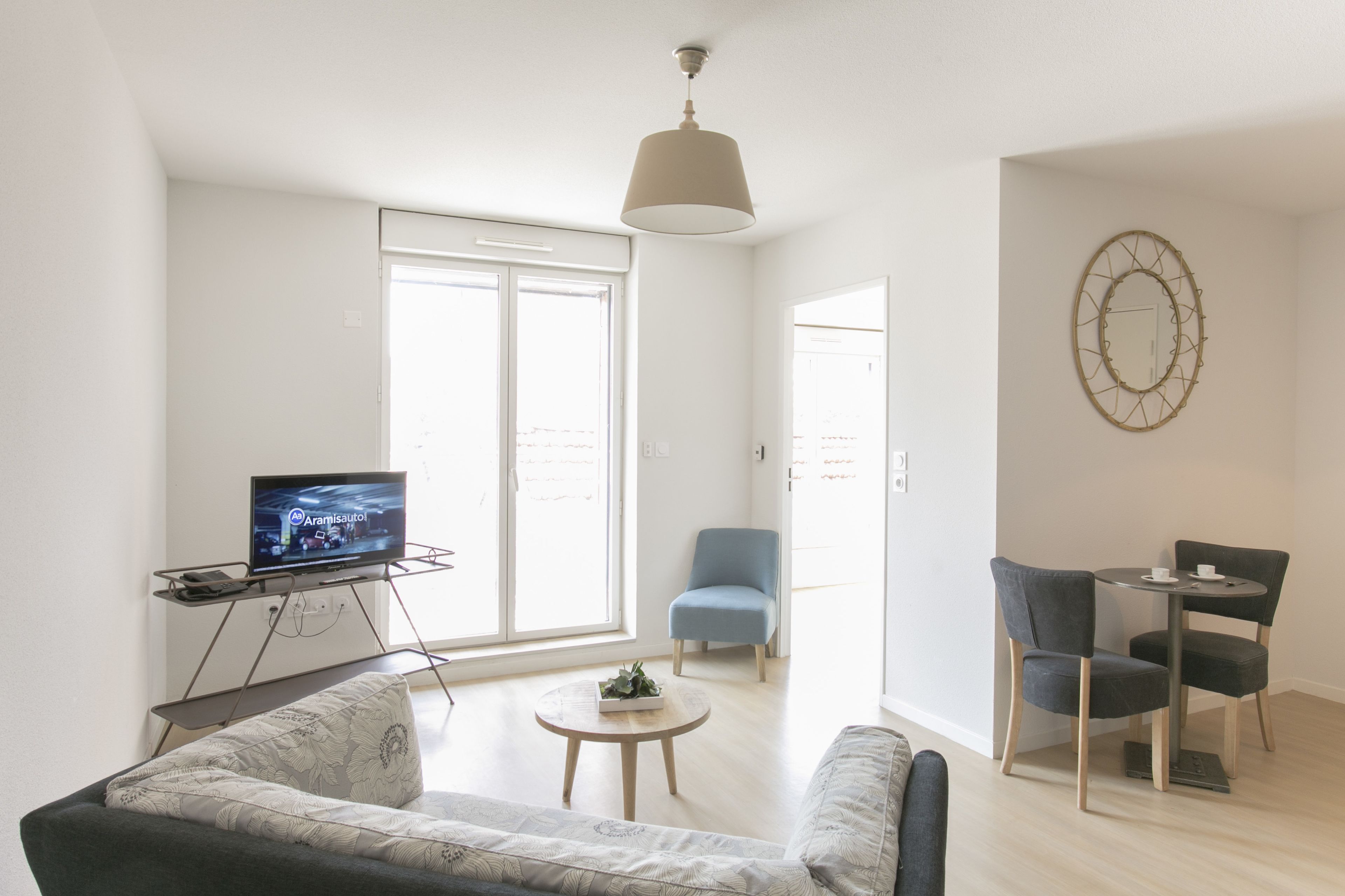 A modern living room with a flat-screen TV, a sofa, a coffee table, and a dining area with chairs.