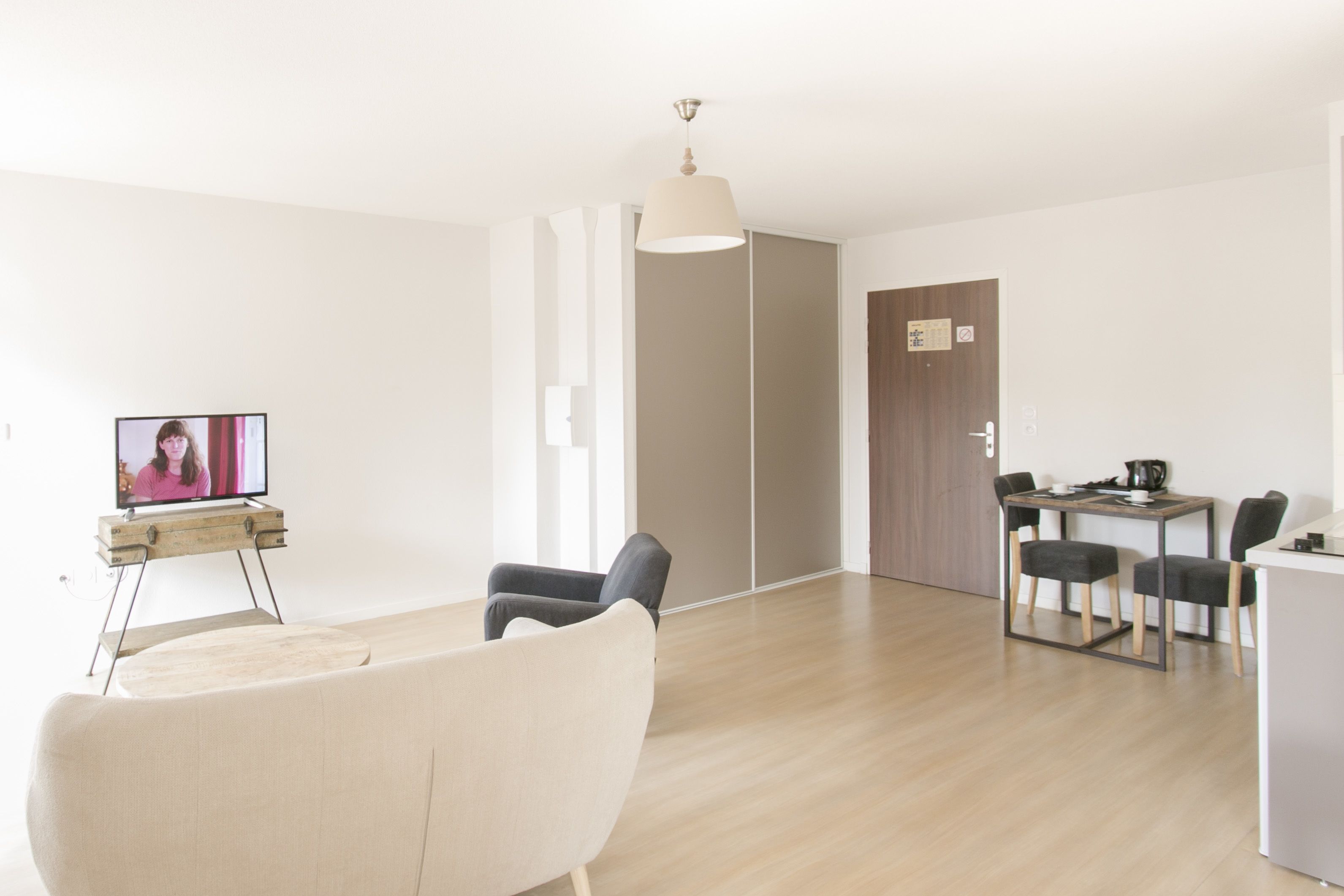Una sala de estar moderna con televisor, un comedor con mesa y sillas, y una lámpara.