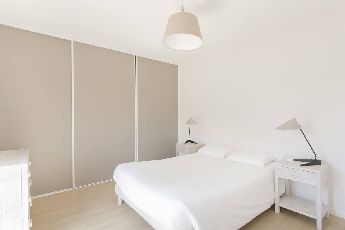 Un dormitorio minimalista con una cama grande, una mesita de noche con lámpara y un armario.