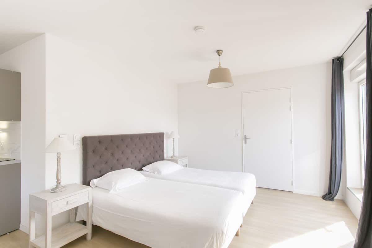 Un dormitorio moderno con una cama grande, una mesita de noche con lámpara, un armario y una ventana con cortinas.