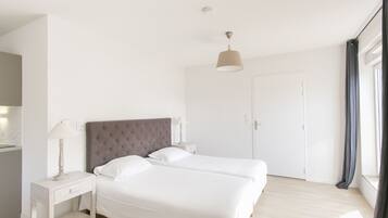 A modern bedroom with a large bed, a bedside table with a lamp, a wardrobe, and a window with curtains.