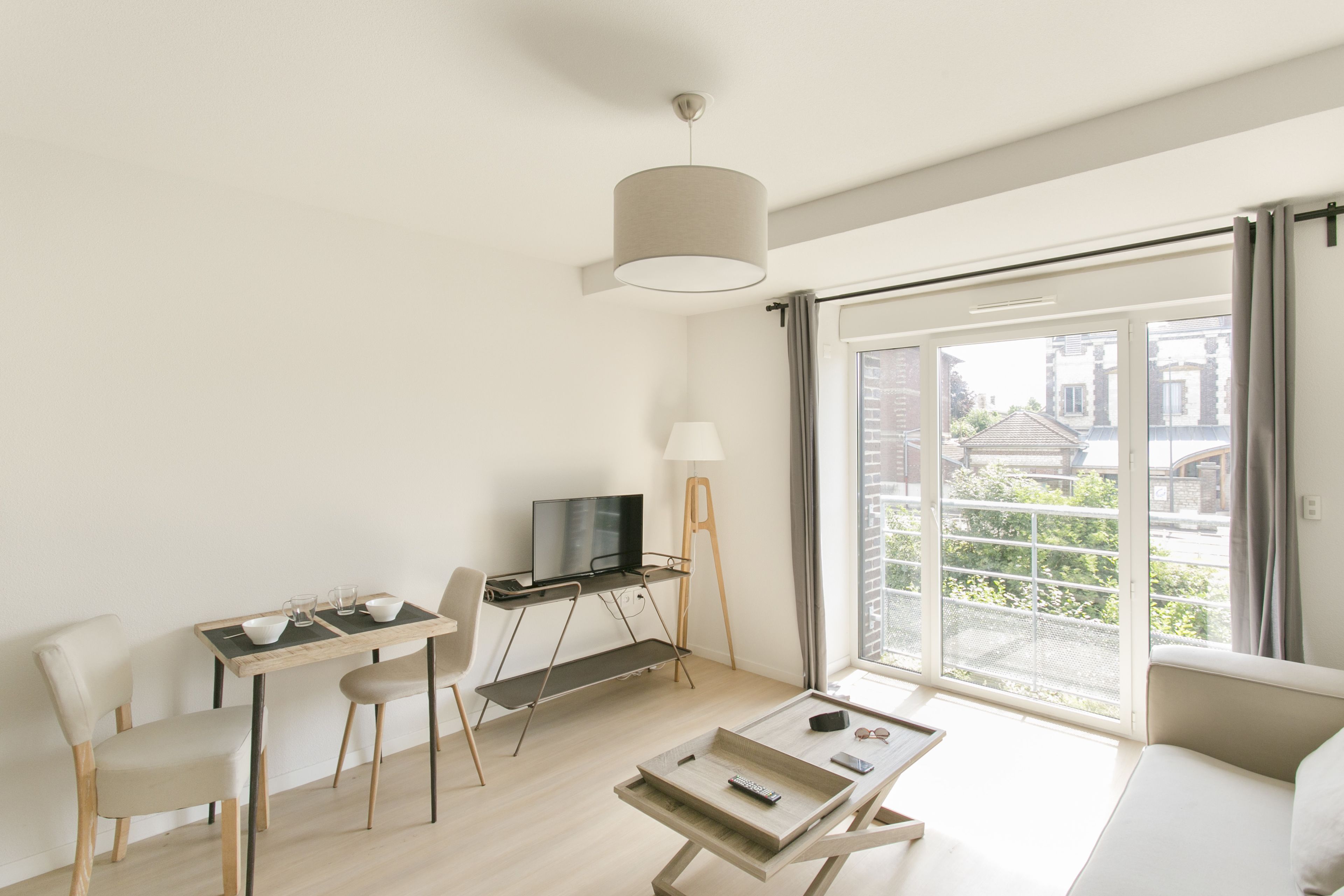 A modern living room with a sofa, a dining table with chairs, a TV, and a balcony with a view of buildings.