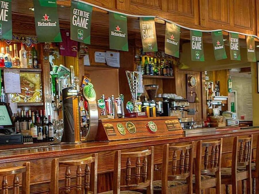 A bar area with multiple Heineken banners, a variety of liquor bottles, and wooden bar stools.