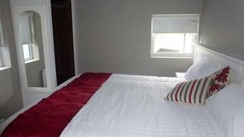 A neatly made bed with a white and red bedspread, a striped pillow, and a window with a view of the outside.