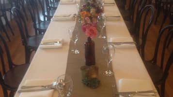 Una larga mesa de comedor con manteles blancos, sillas negras y un centro de mesa floral.