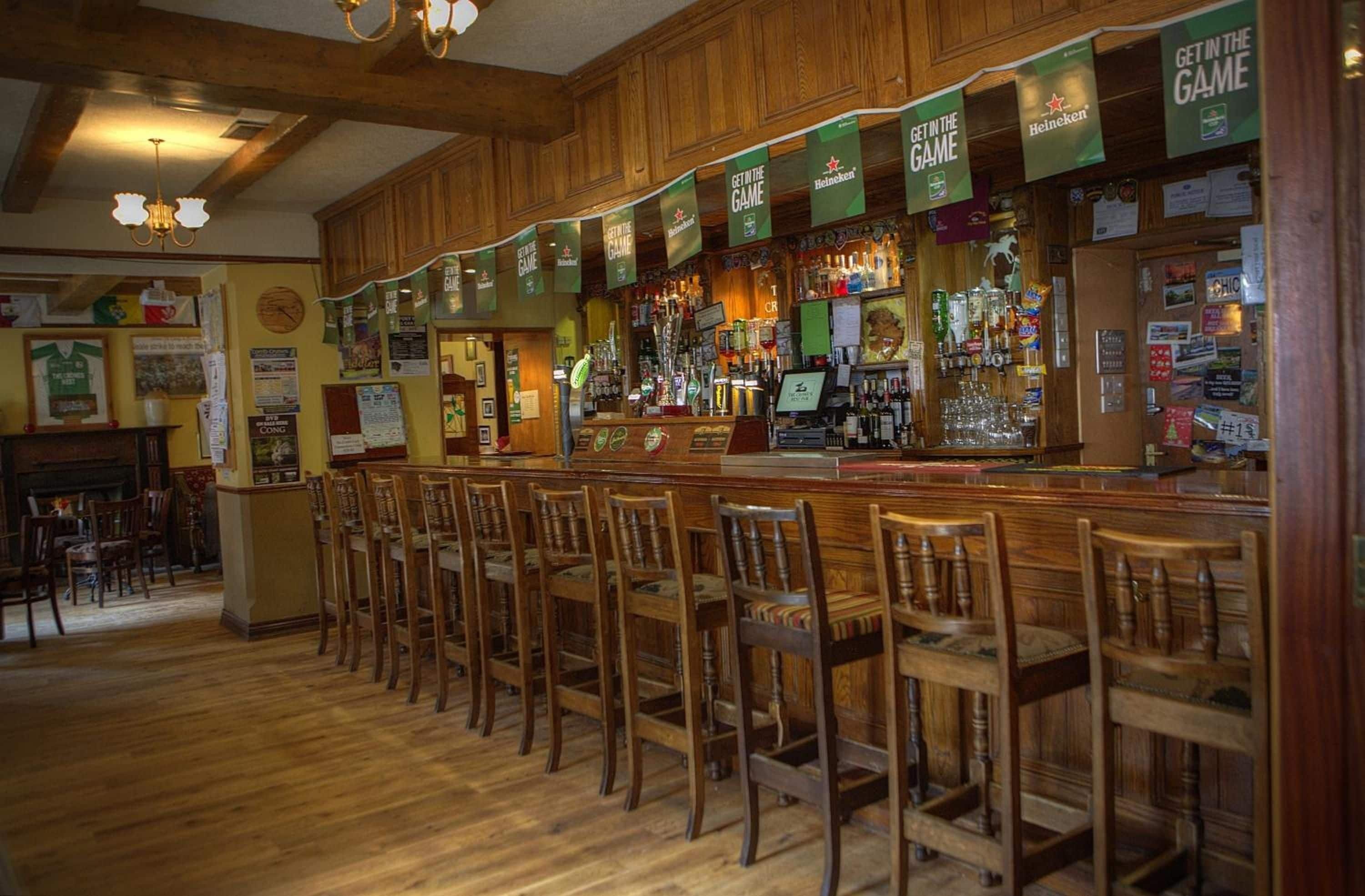 Área de bar com banquetas de madeira e um balcão exibindo diversas garrafas.