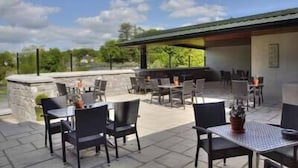 An outdoor patio with stone flooring, black metal tables, and chairs. - Ryan's Hotel (Cong)