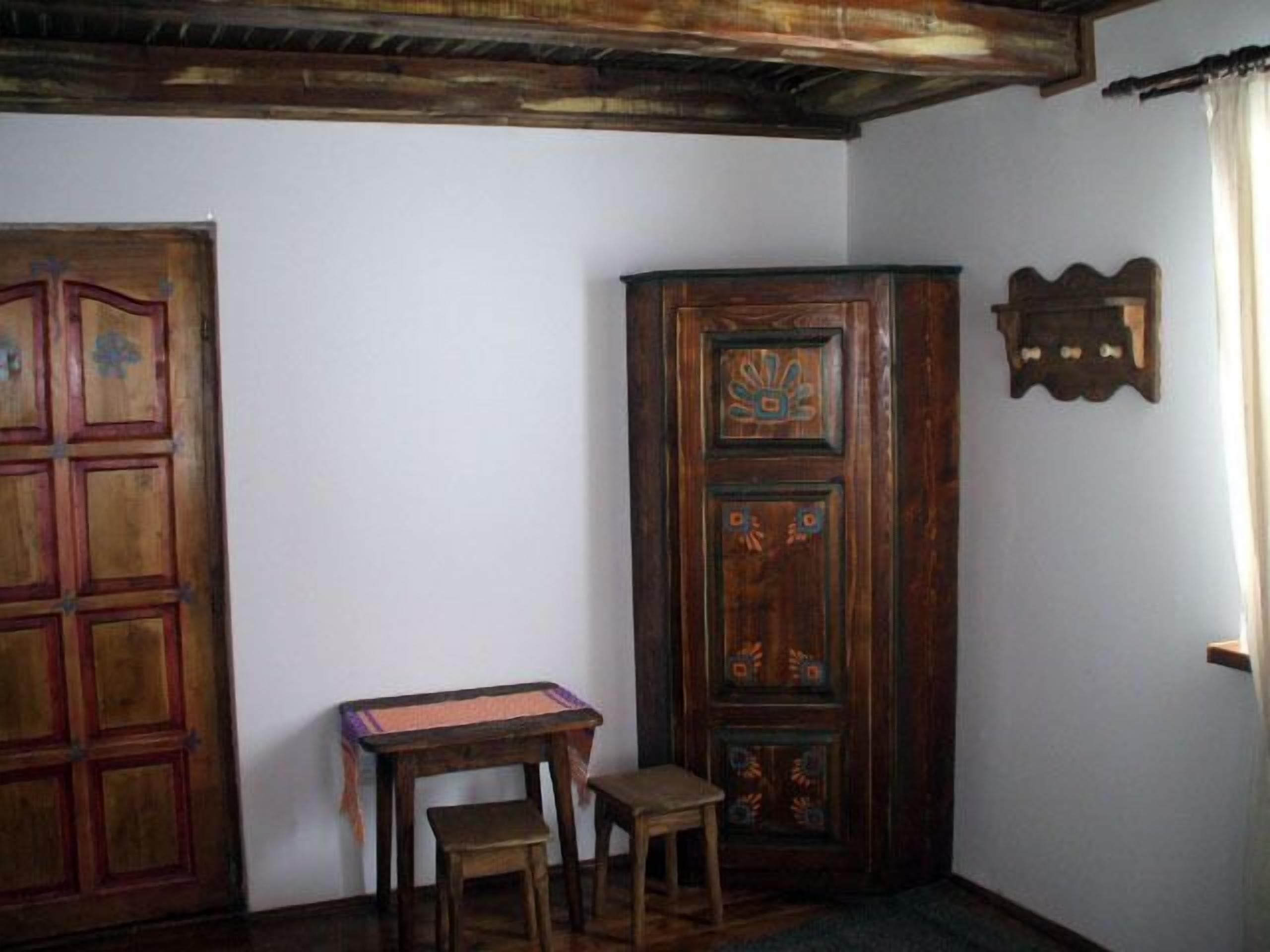 A room with a wooden door, a cabinet with decorative panels, a small table with a chair, and a window with curtains.