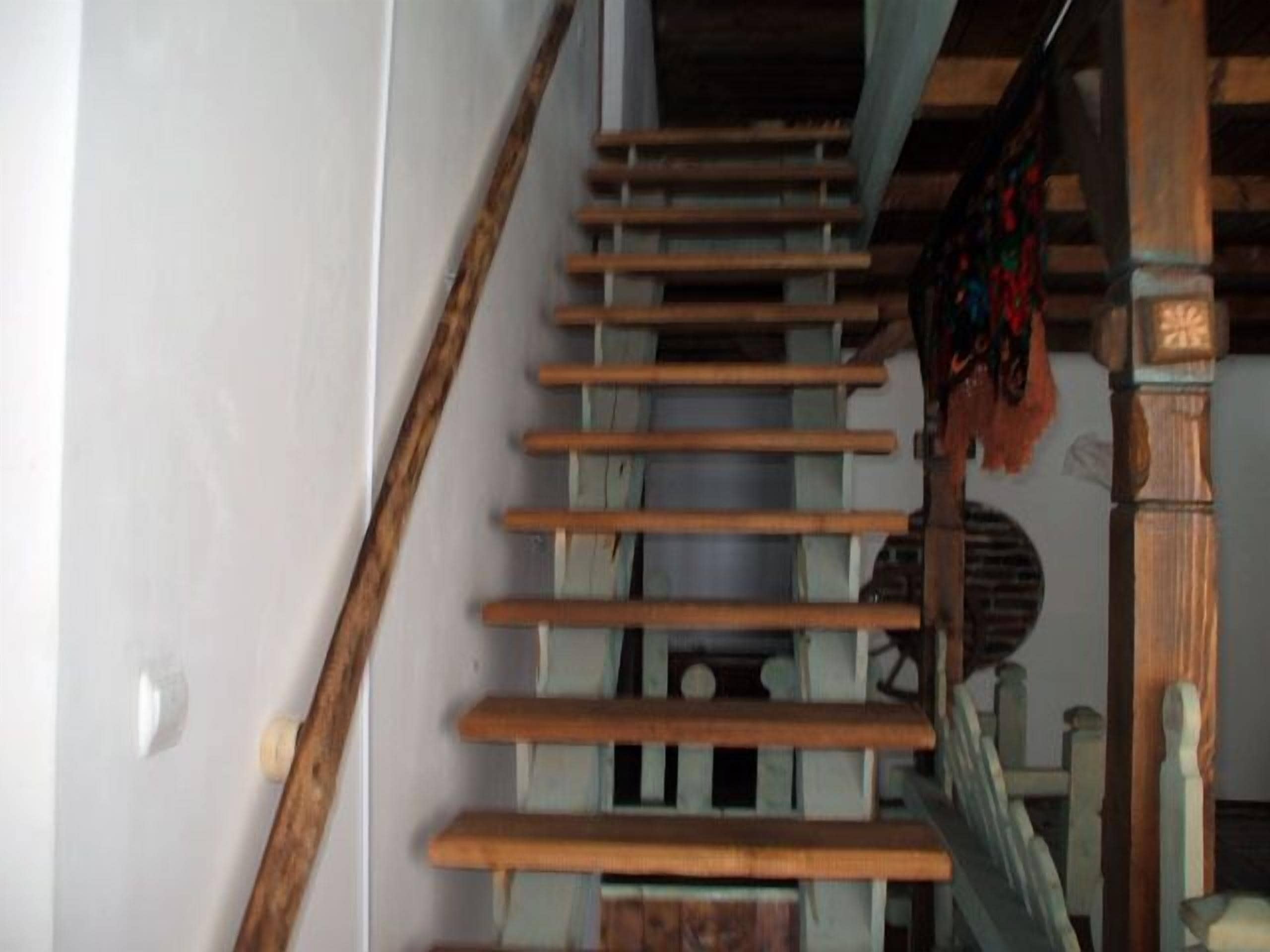 A wooden staircase with a handrail, leading to a landing with a patterned rug.