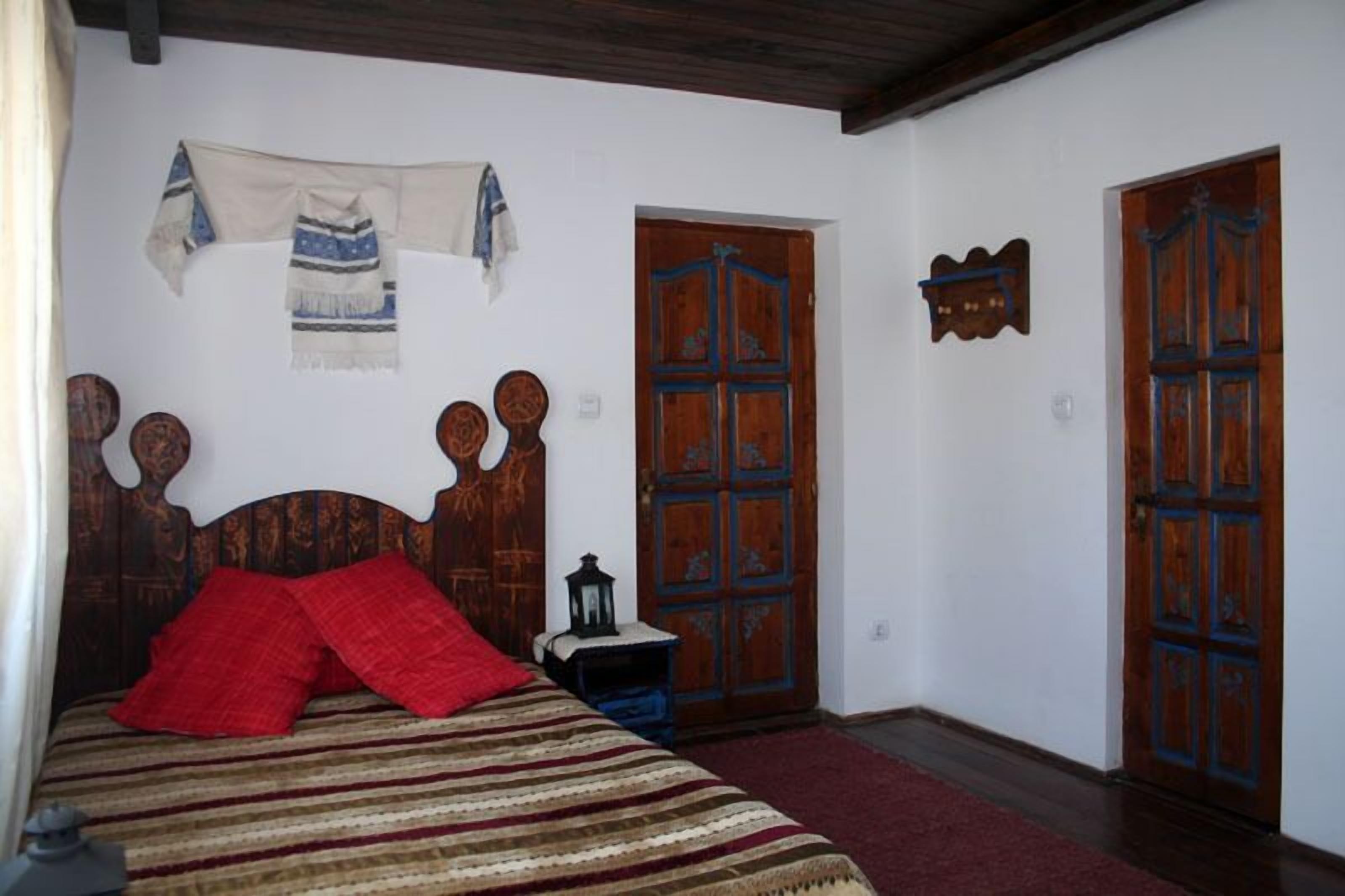 Quarto com cama de madeira, almofadas vermelhas, manta listrada e duas portas de madeira.