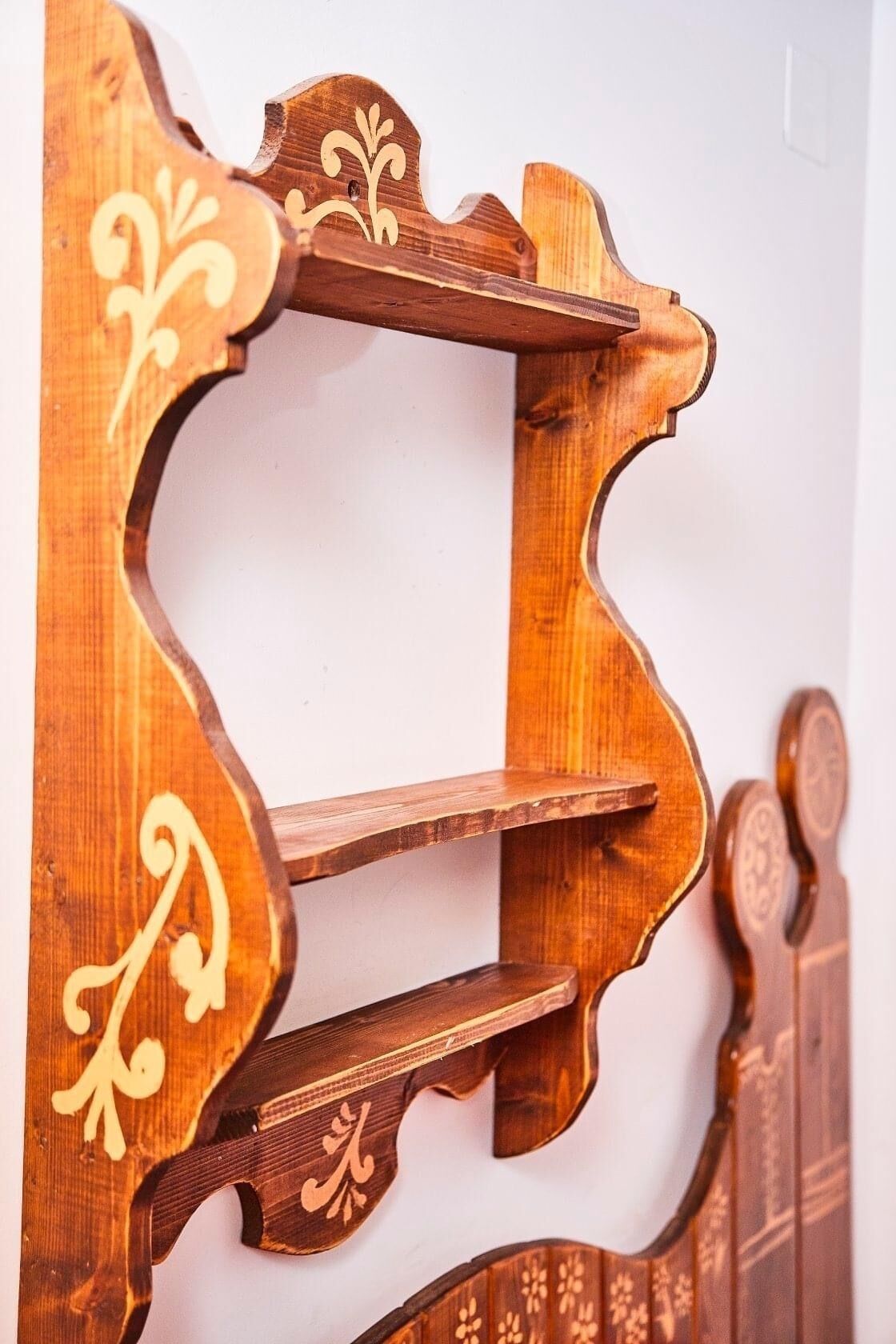 A wooden wall-mounted shelf unit with ornate carvings and two shelves.