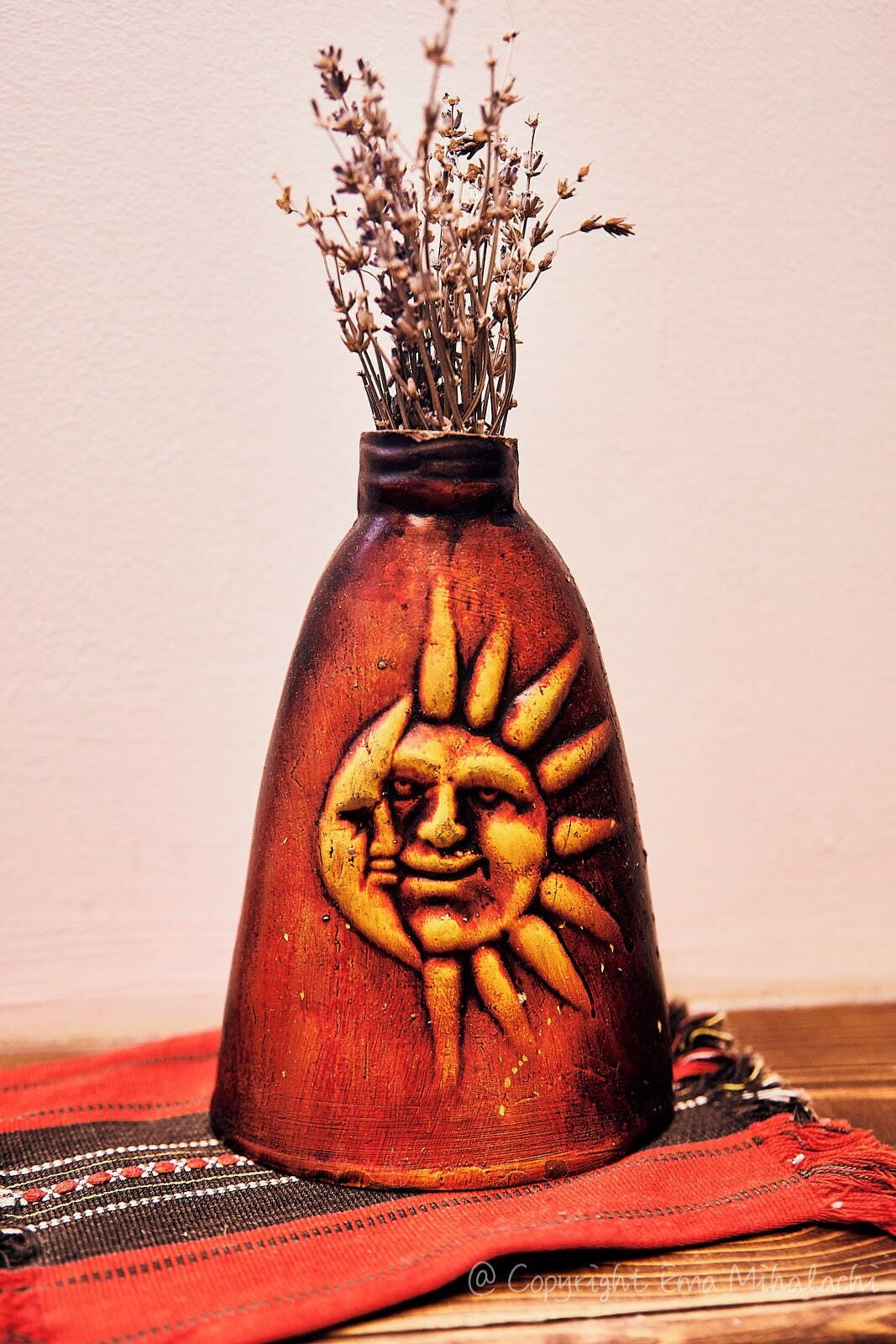 Un jarrón con un diseño tallado de sol y flores secas.