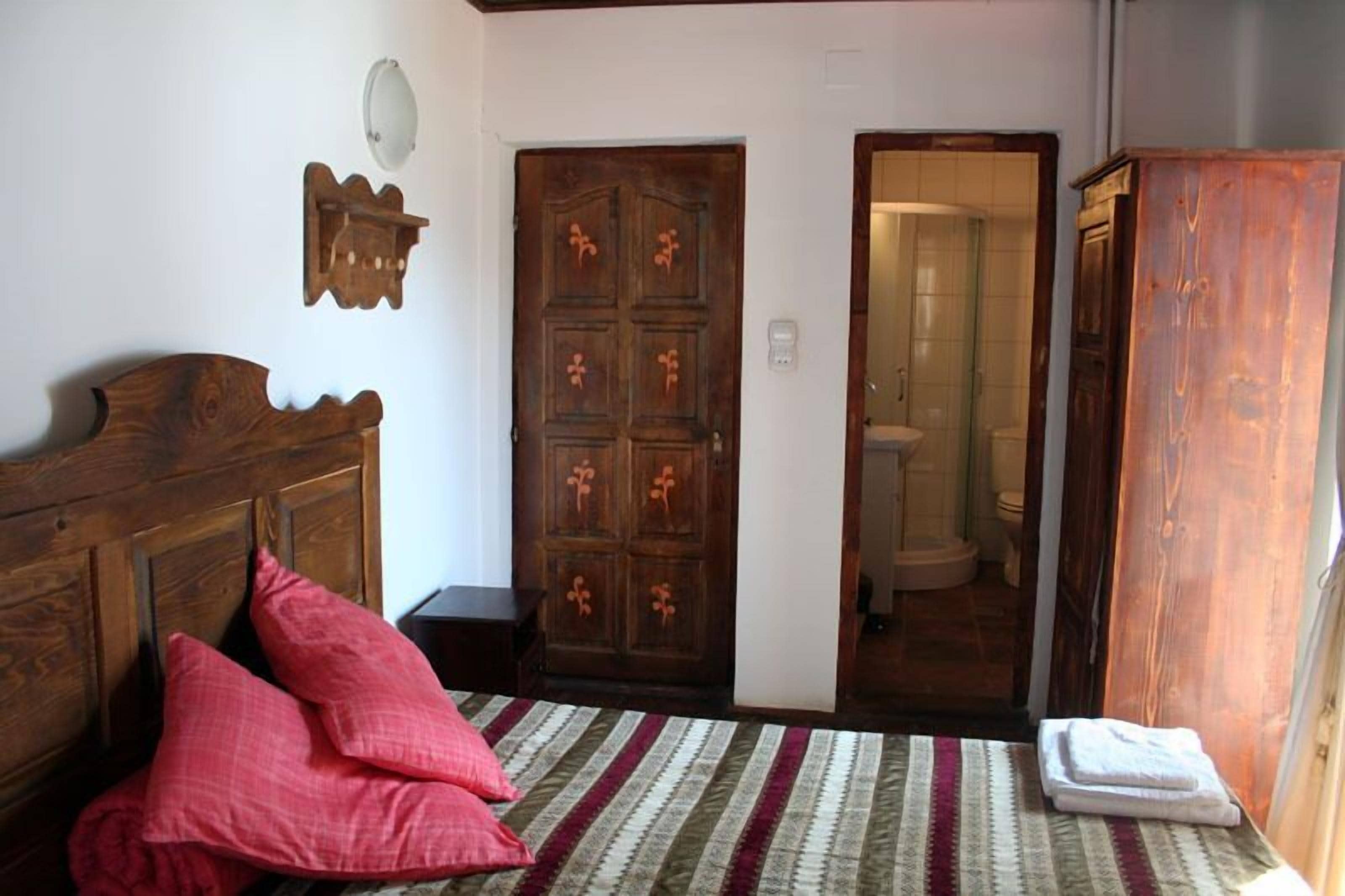 A bedroom with a wooden bed, a large wardrobe, and a door leading to a bathroom.