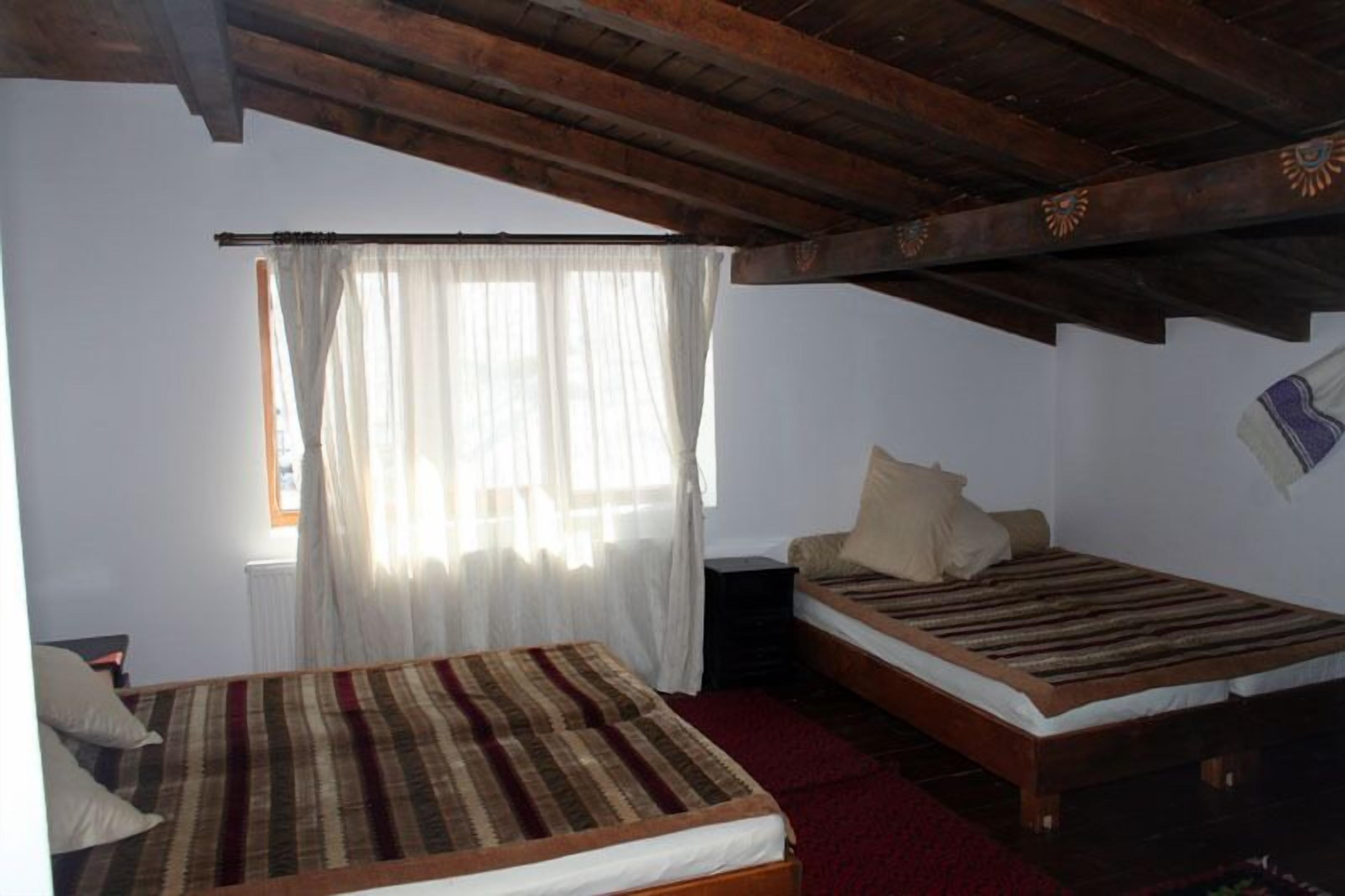 A room with two beds, a window with sheer curtains, and a wooden ceiling.