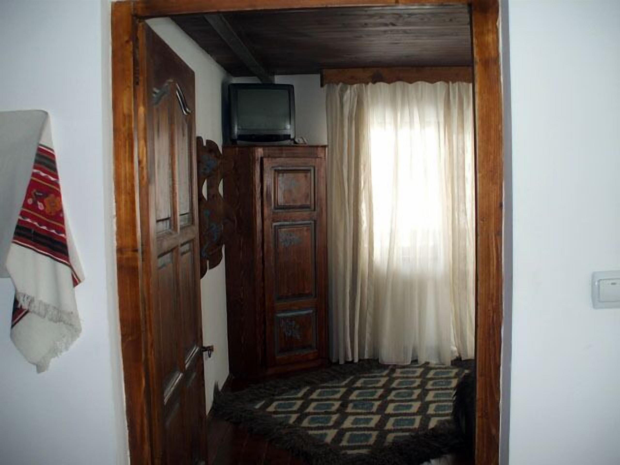 A room with a wooden wardrobe, a television on top, a patterned rug, and a white curtain.