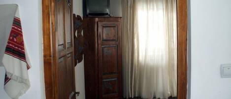 A room with a wooden wardrobe, a television on top, a patterned rug, and a white curtain.