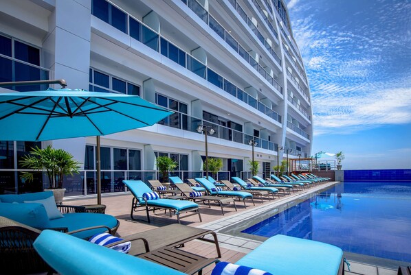 A poolside area with lounge chairs and umbrellas, a modern building with large windows, and a clear sky.